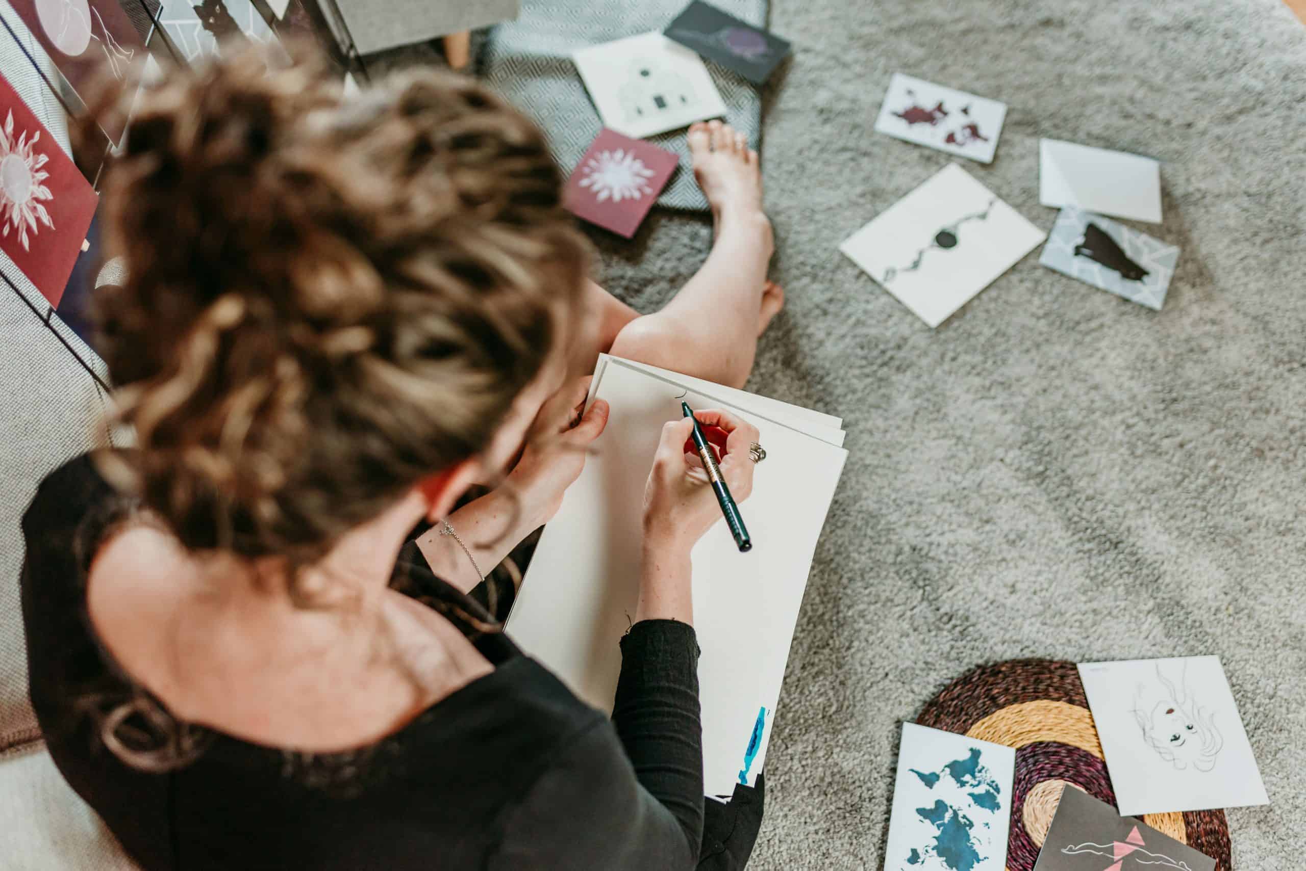Heads Together. Image from above shows Tamzin sitting on the floor, drawing, with some of her artwork scattered around her.