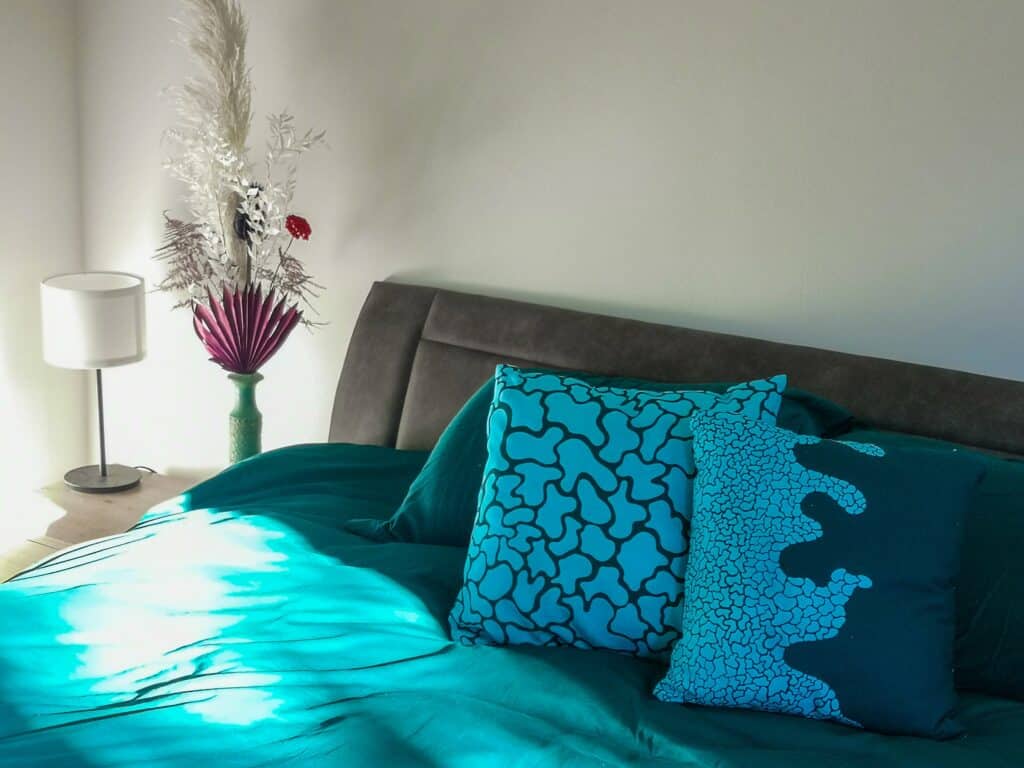 Bed with jewel green bedspread and two light blue cushions