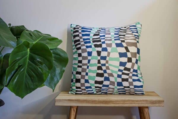 Cushion on a bench next to a plant, cushion has wavey pattern in blue, mint green, grey and and black