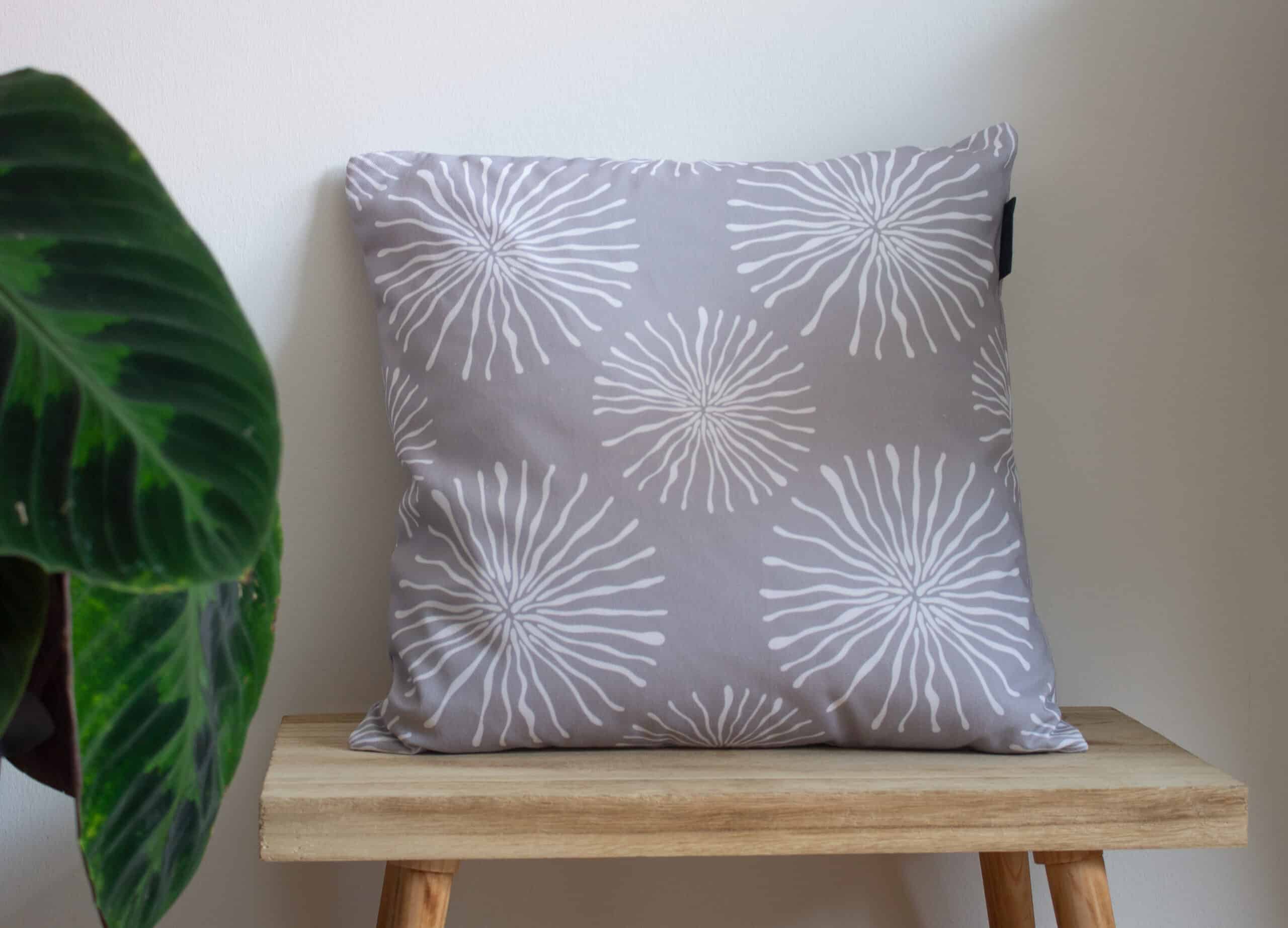 Grey Throw cushion with white circular pattern design on a bench with a plant