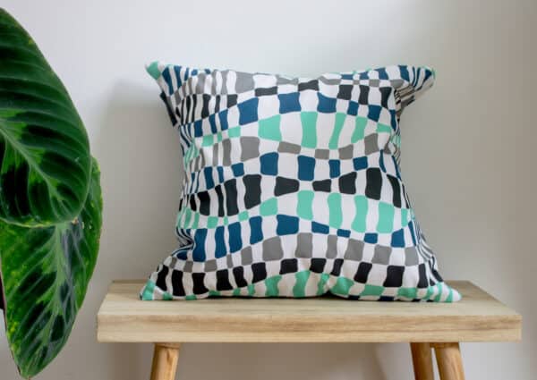 Wave Throw Cushion Green and Blue Wave Flowing Pattern Design on a bench with a plant