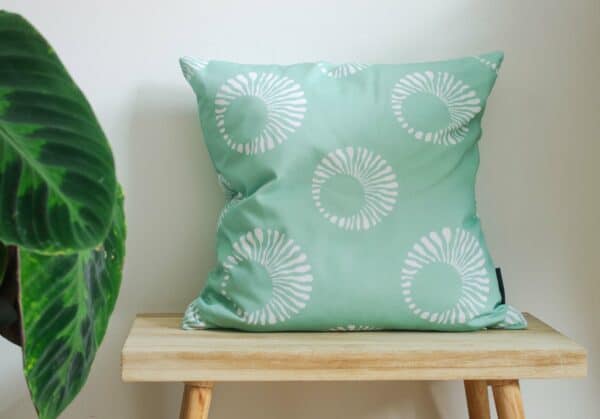 Mint green Throw Cushion with white pattern on a bench with a plant
