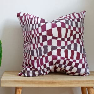 Pink Throw Cushion with purple flowing wave pattern design on a bench with a plant