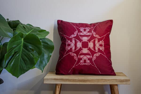 Red Throw Cushion with white symmetrical design on a bench with a plant